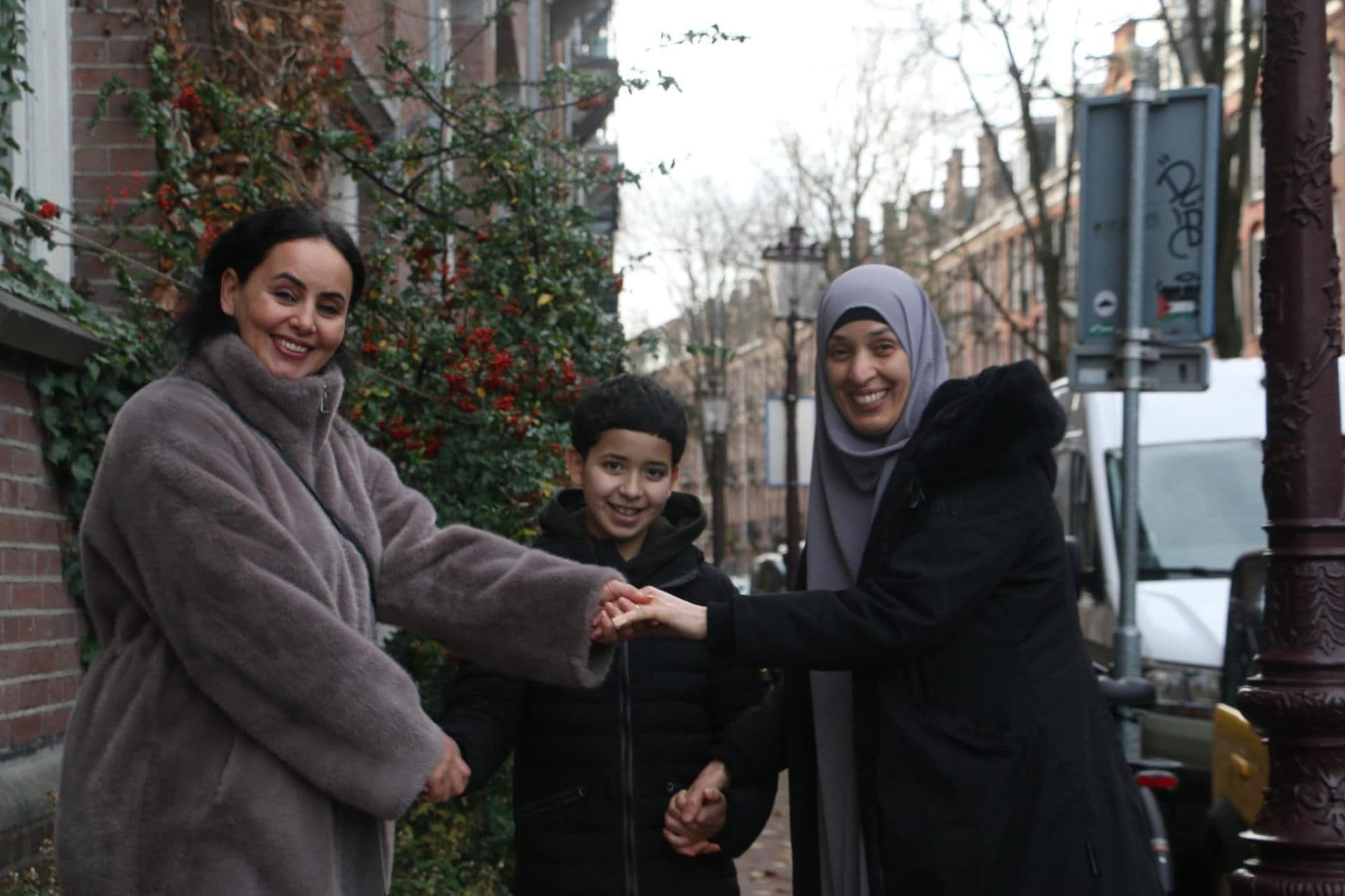 Twee moeders en een kind houden samen handen vast in een Amsterdamse straat